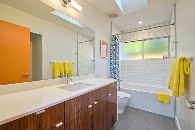 Bathroom in Aa House by Lloyd Russell AIA features a wooden vanity with white countertop and a bathtub under a frosted window.