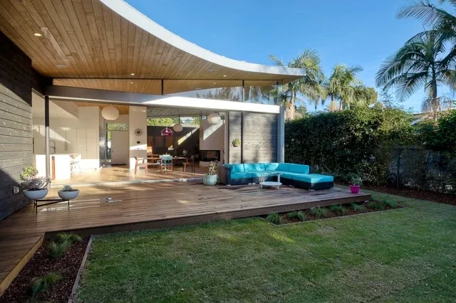 The Aa House features a covered patio with a wooden ceiling overhang and vibrant blue outdoor seating.
