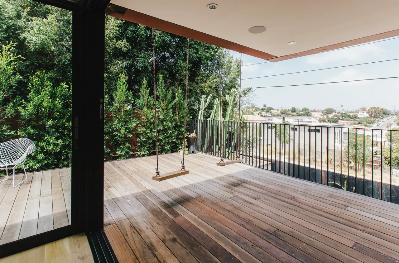 Outdoor wooden deck patio with swings, metal railing, and green landscaping overlooking an urban area.