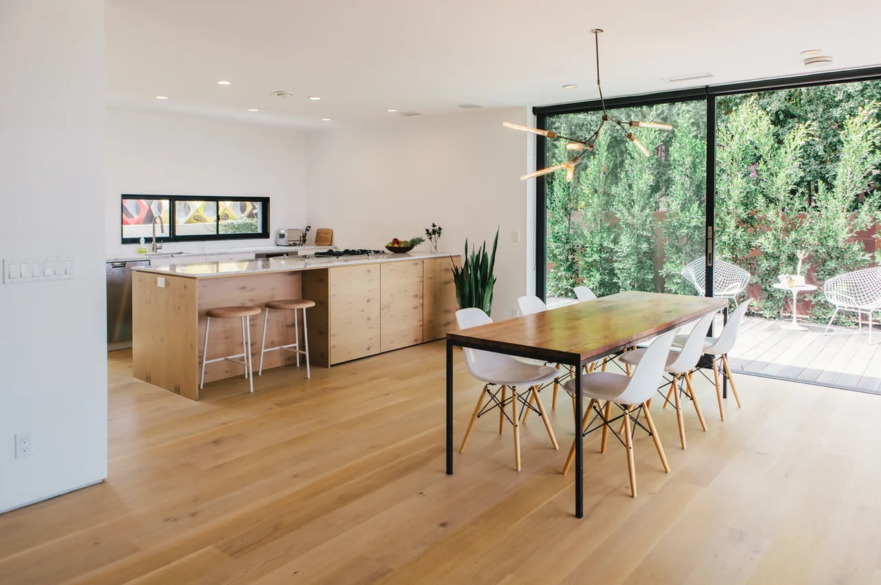 Open plan kitchen and dining area with wood floors, a wood island with stools, and sliding glass doors to a green outdoor space.