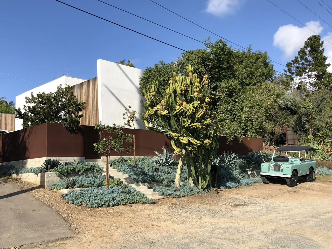 Modern home at 32nd Street with white walls, vertical wood slats, and rust-colored metal fencing in a landscaped setting.