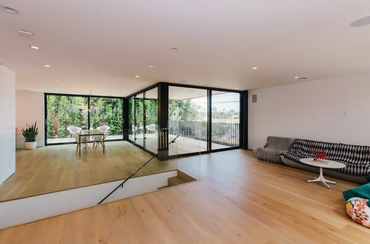 Open plan living and dining space with floor-to-ceiling sliding glass doors opening to balcony and wood flooring.