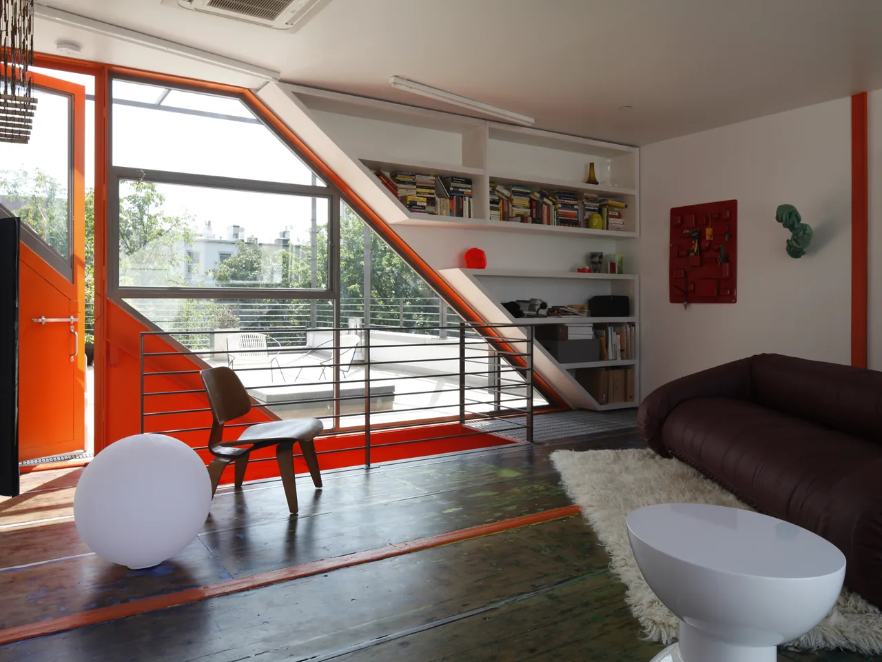 A living area featuring an orange metal-framed window and door with built-in shelving and a brown sofa.
