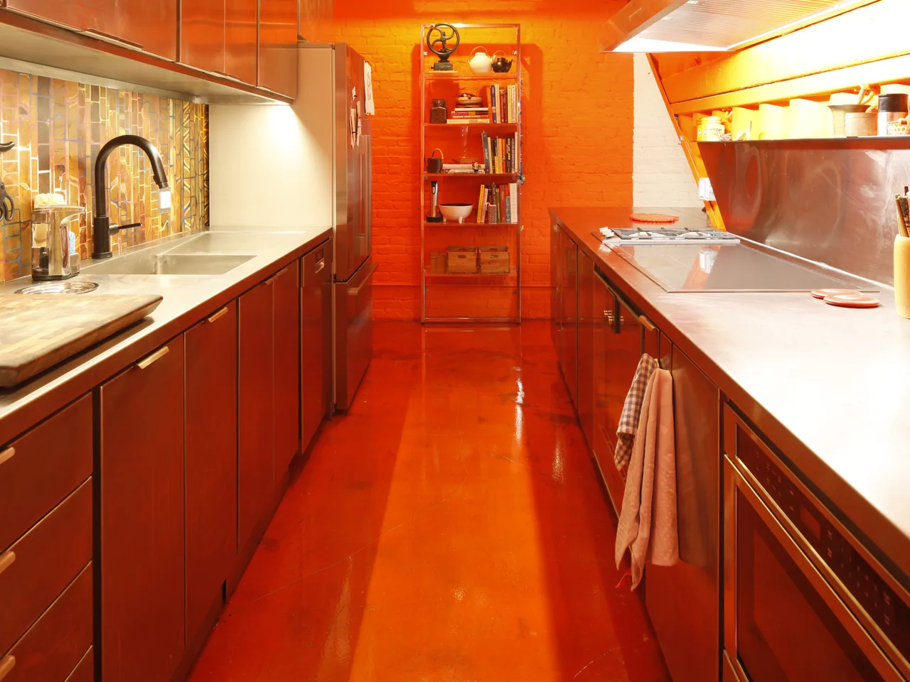 Galley kitchen with stainless steel counters, a gas range, and orange walls and flooring.