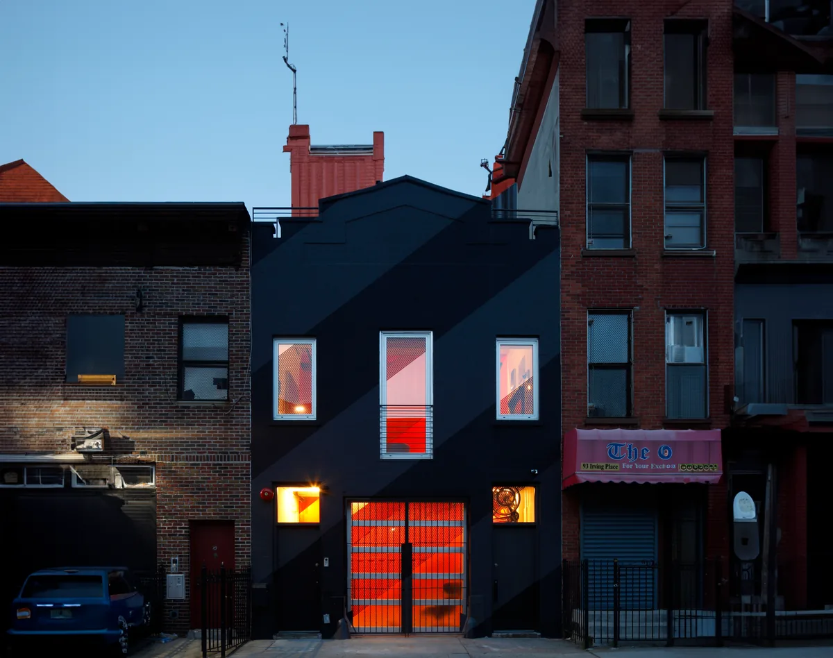 The IRVING PLACE CARRIAGE HOUSE features a black exterior with illuminated red interiors visible through its windows and gate.