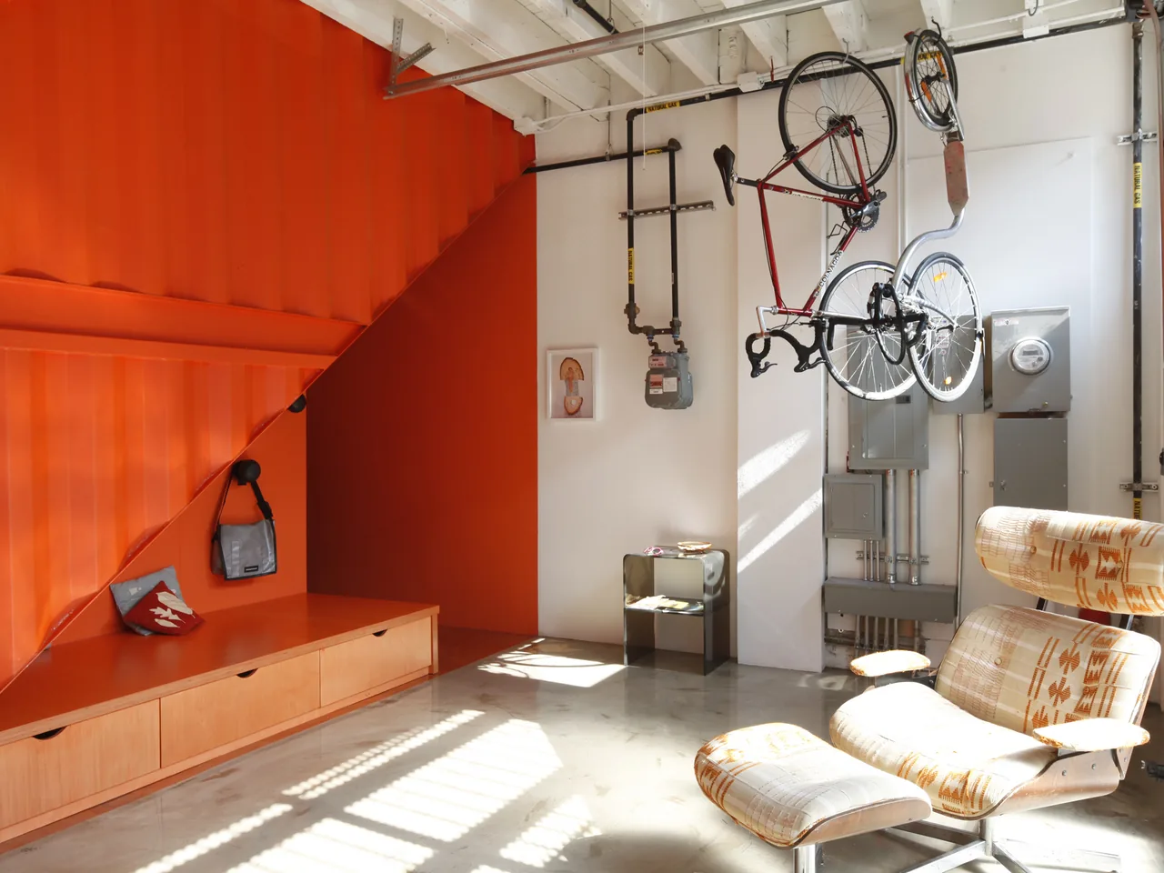 Room features a corrugated orange stairway with built-in storage and a suspended bicycle over a polished concrete floor.