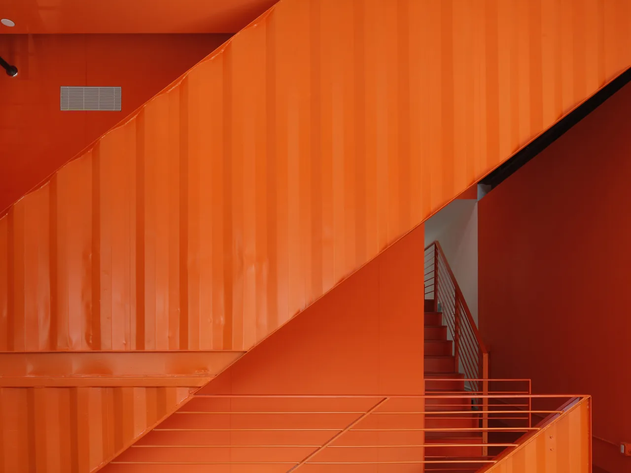 Bright orange metal staircase with matching orange walls and railings.