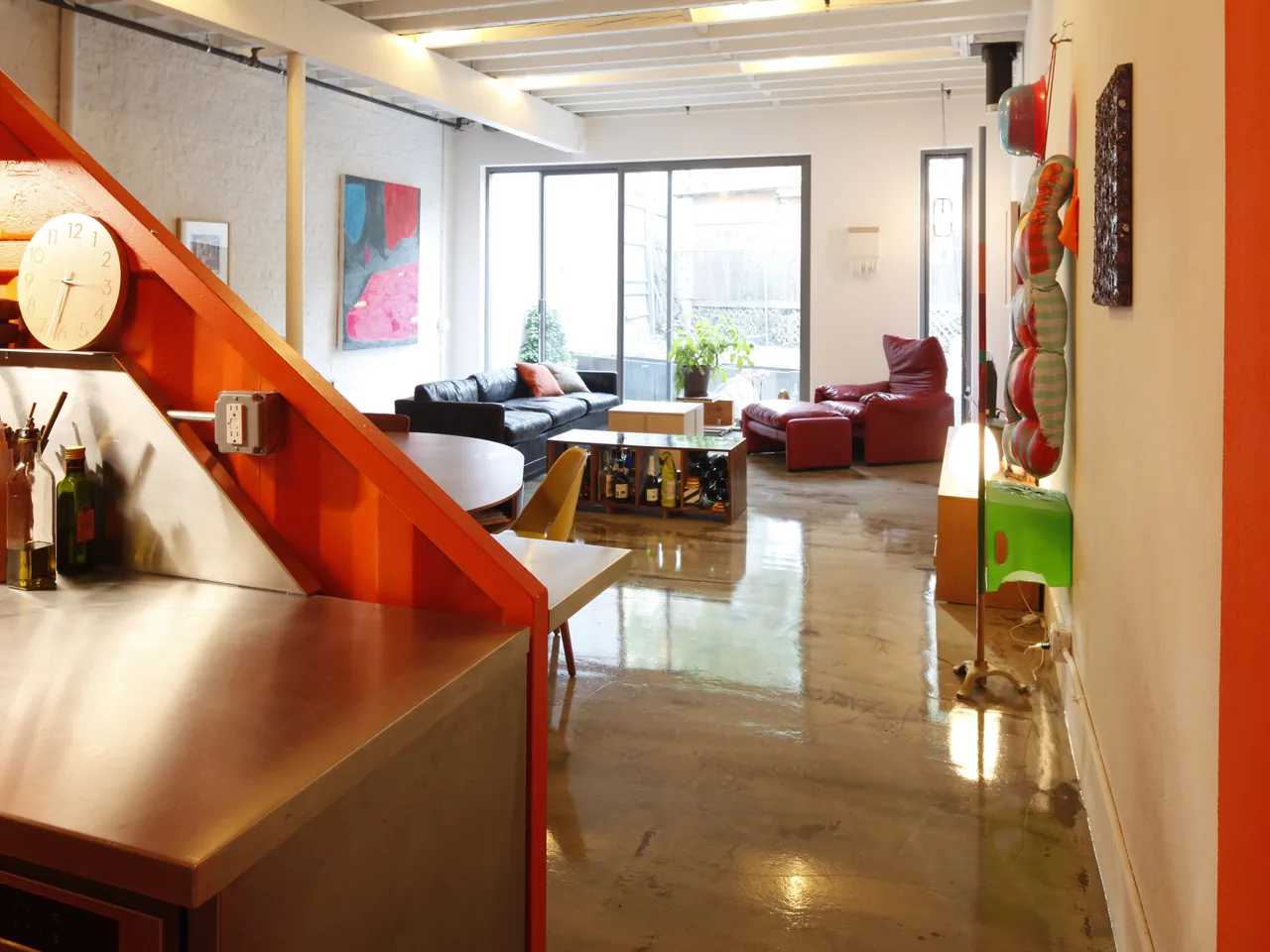 Living room area with polished concrete floors, an orange staircase, and sliding glass doors opening to an outdoor space.