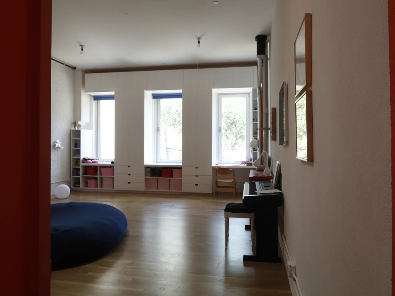 White built-in shelves surround three large windows in this bright room with wooden flooring.