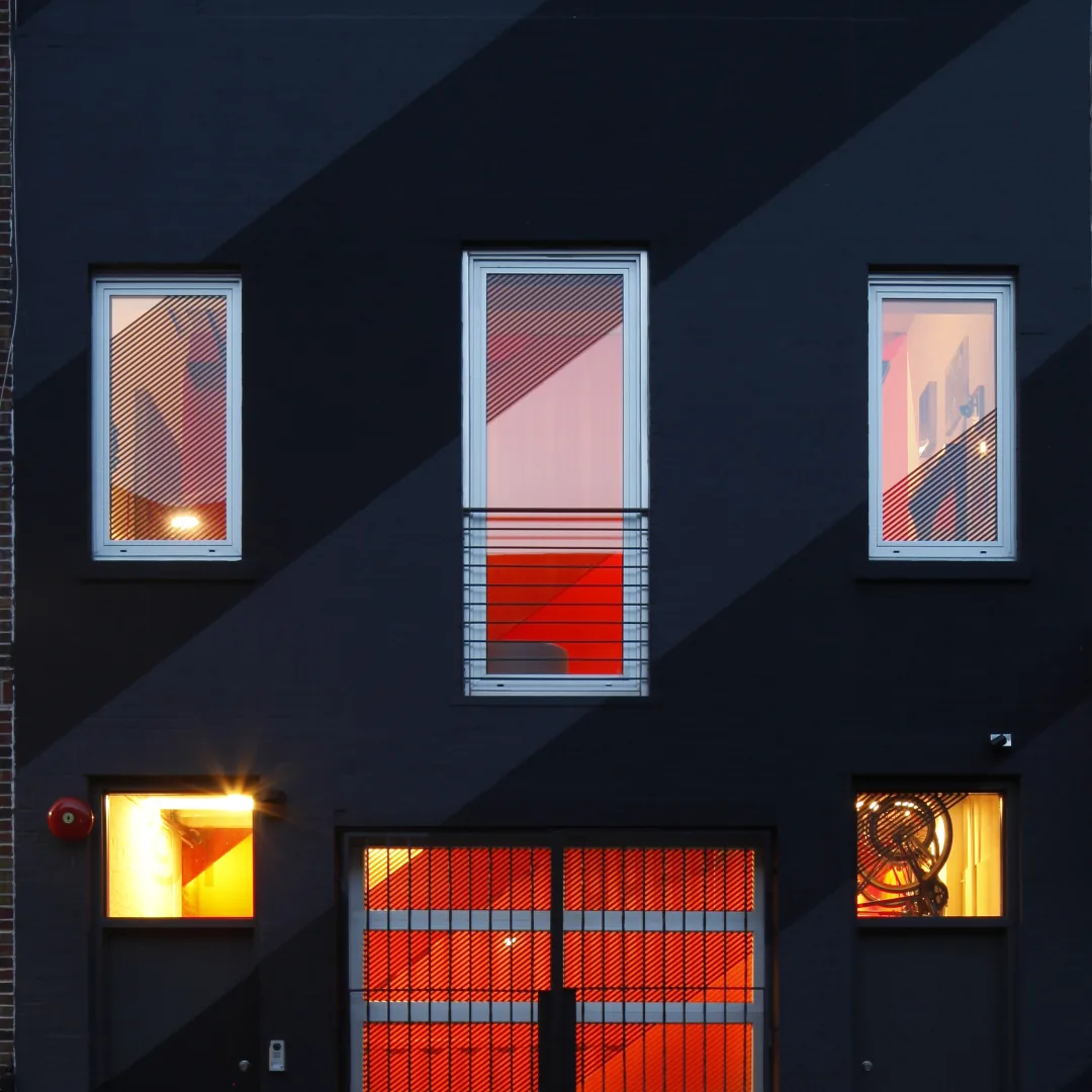 IRVING PLACE CARRIAGE HOUSE features a black facade with striking illuminated red interiors in an urban setting.