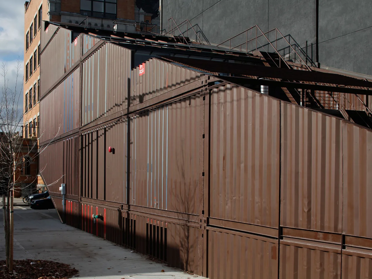 CARROLL HOUSE features a shipping container facade with exterior metal staircase on an urban corner site in New York.