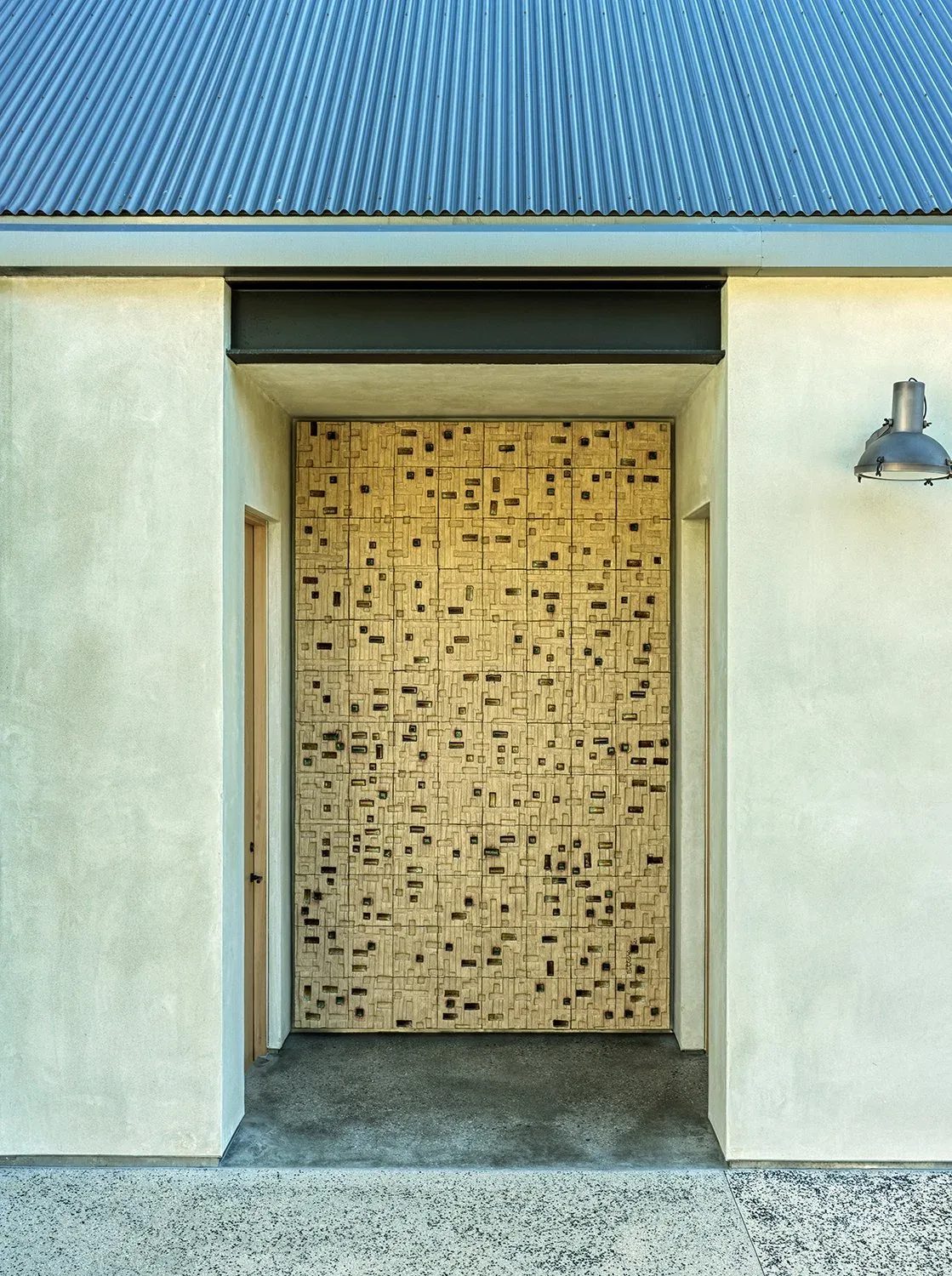 Recessed front entry with textured concrete walls, a unique wooden door panel, and a metal sloped roof above.