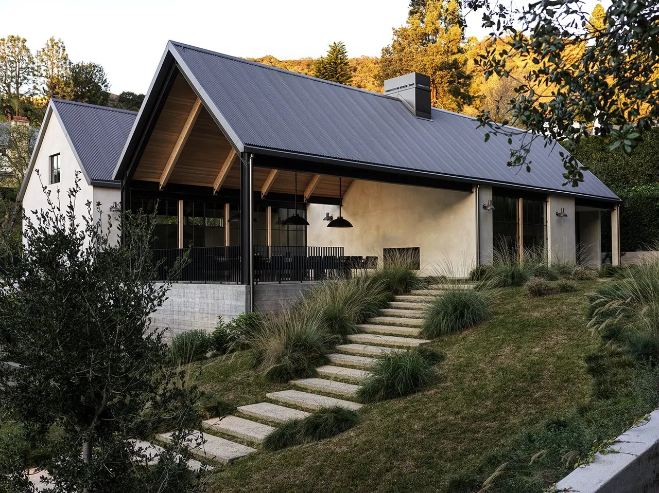 Canyon House features a gable corrugated metal roof and concrete stairs leading to an elevated patio with outdoor dining in Los Angeles.