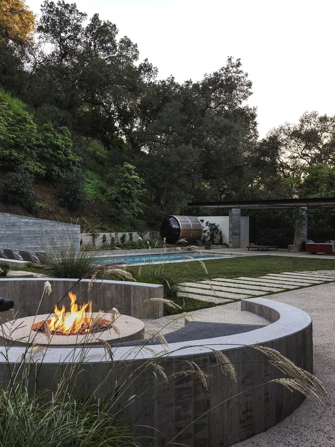 The Canyon House outdoor patio features a curved concrete fire pit with seating, a pool, and natural hillside landscaping.