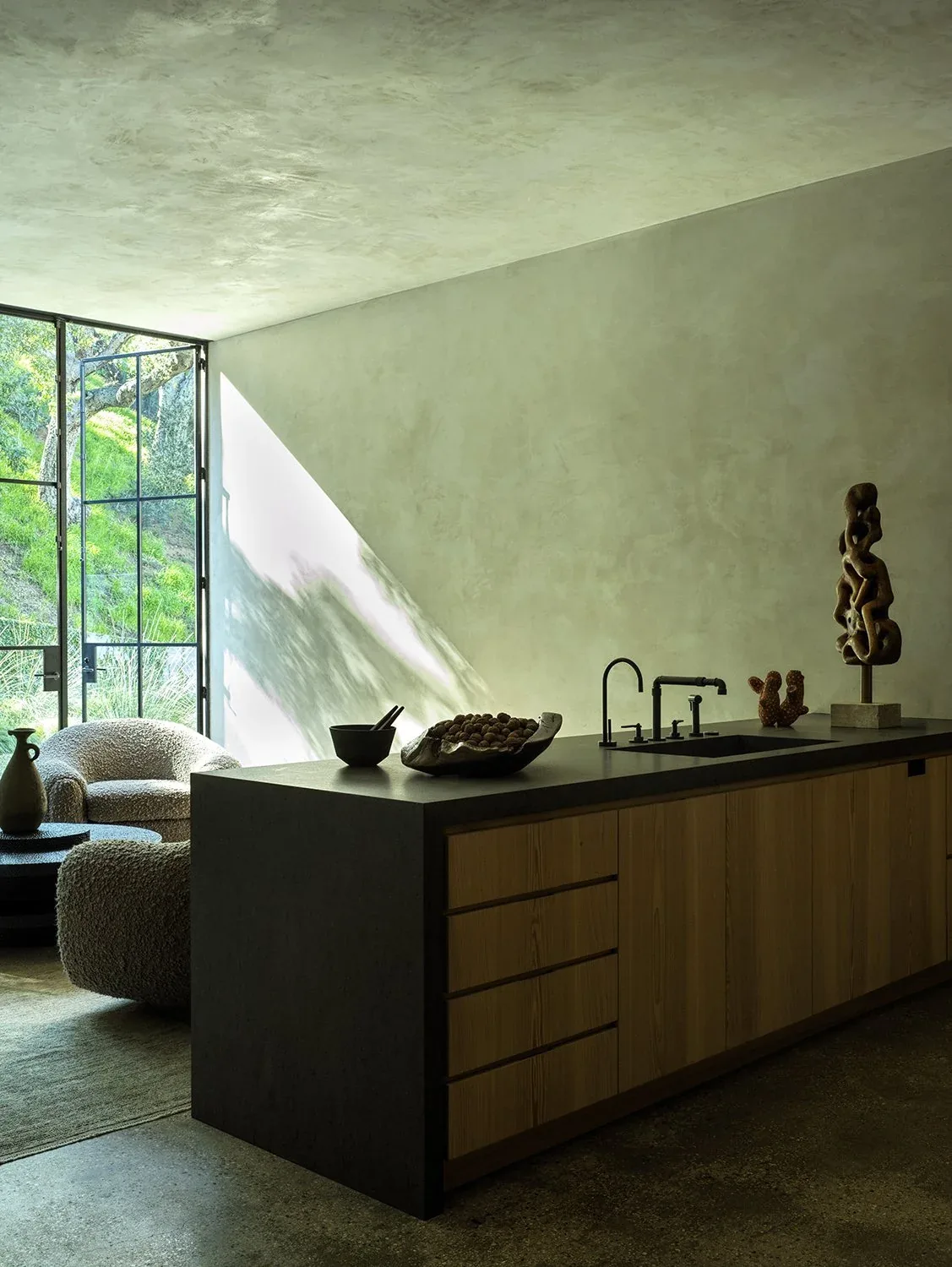 Modern kitchen island with wooden cabinetry, black countertop and matte black fixtures, adjoining a seating area with varied textures.