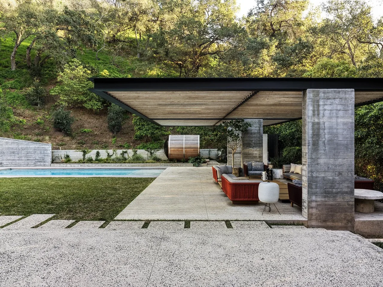 The outdoor living space at Canyon House features concrete seating, a pool, and a hillside backdrop under a flat roof canopy.