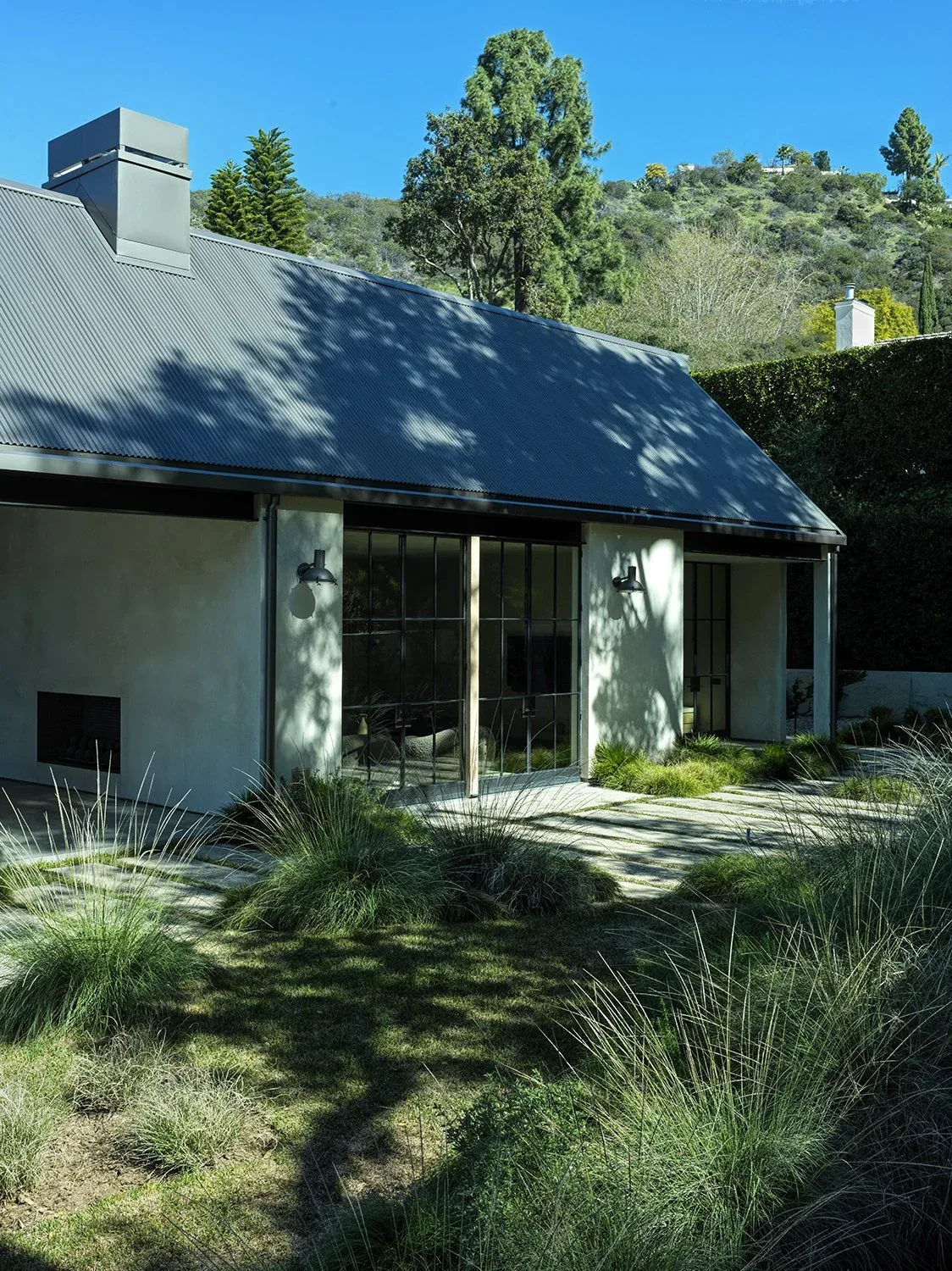 The Canyon House features a textured concrete finish with large black metal-framed glass doors and a sloped metal roof.