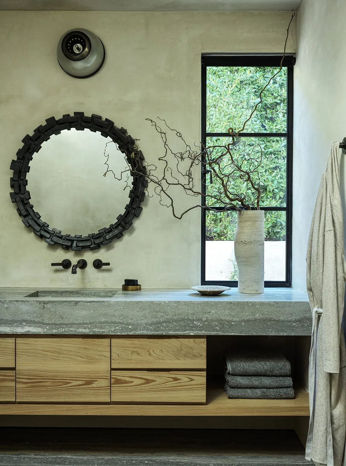 Concrete countertop and wood cabinetry complement a black-framed mirror and window in this bathroom sink area.