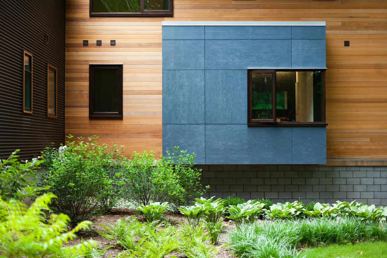 The Pigeon Creek Residence features wood siding with a contrasting blue panel detail and landscaped greenery in front.
