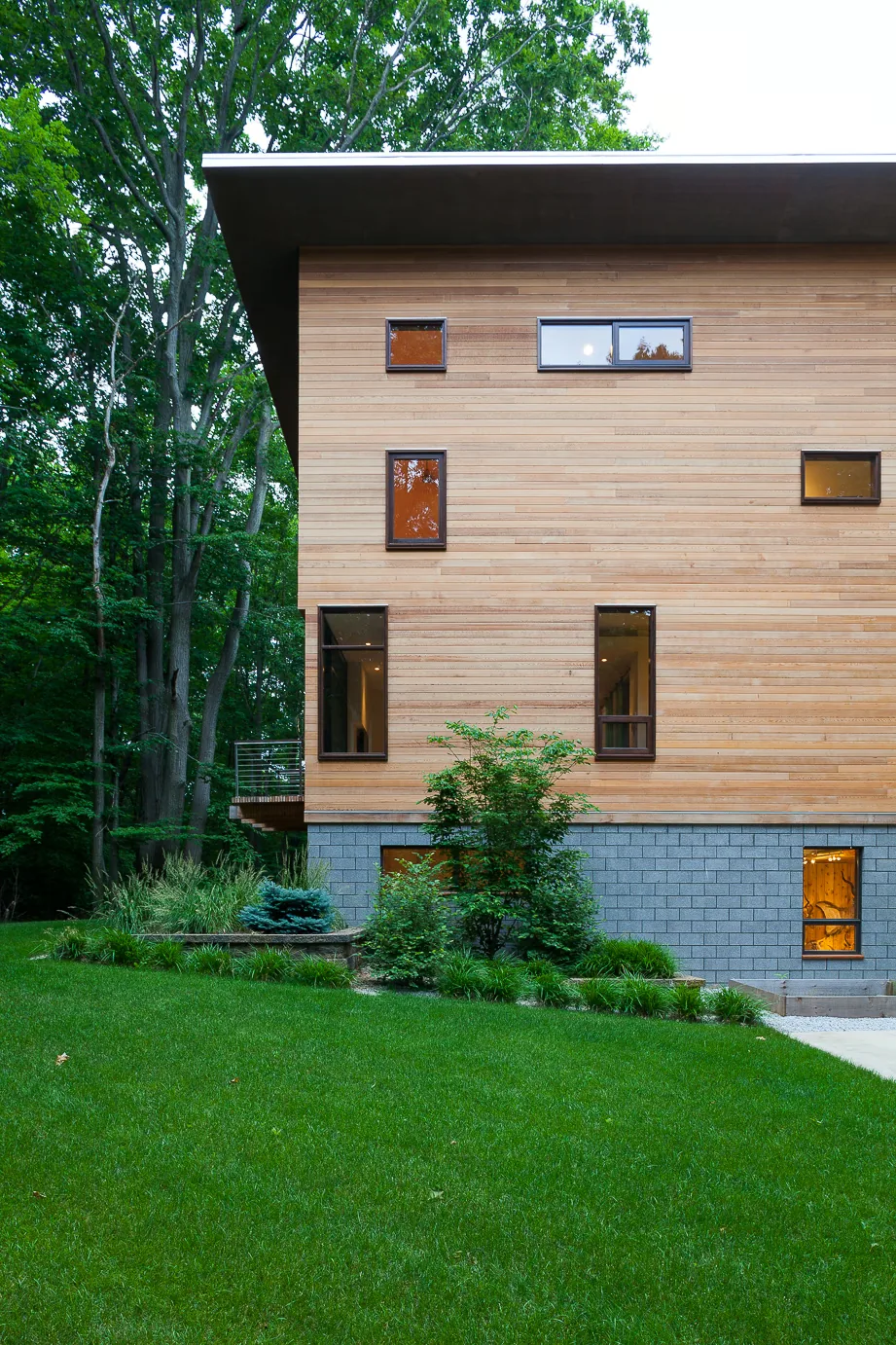 Modern house exterior with horizontal wood siding and varied window sizes above a grey block foundation.