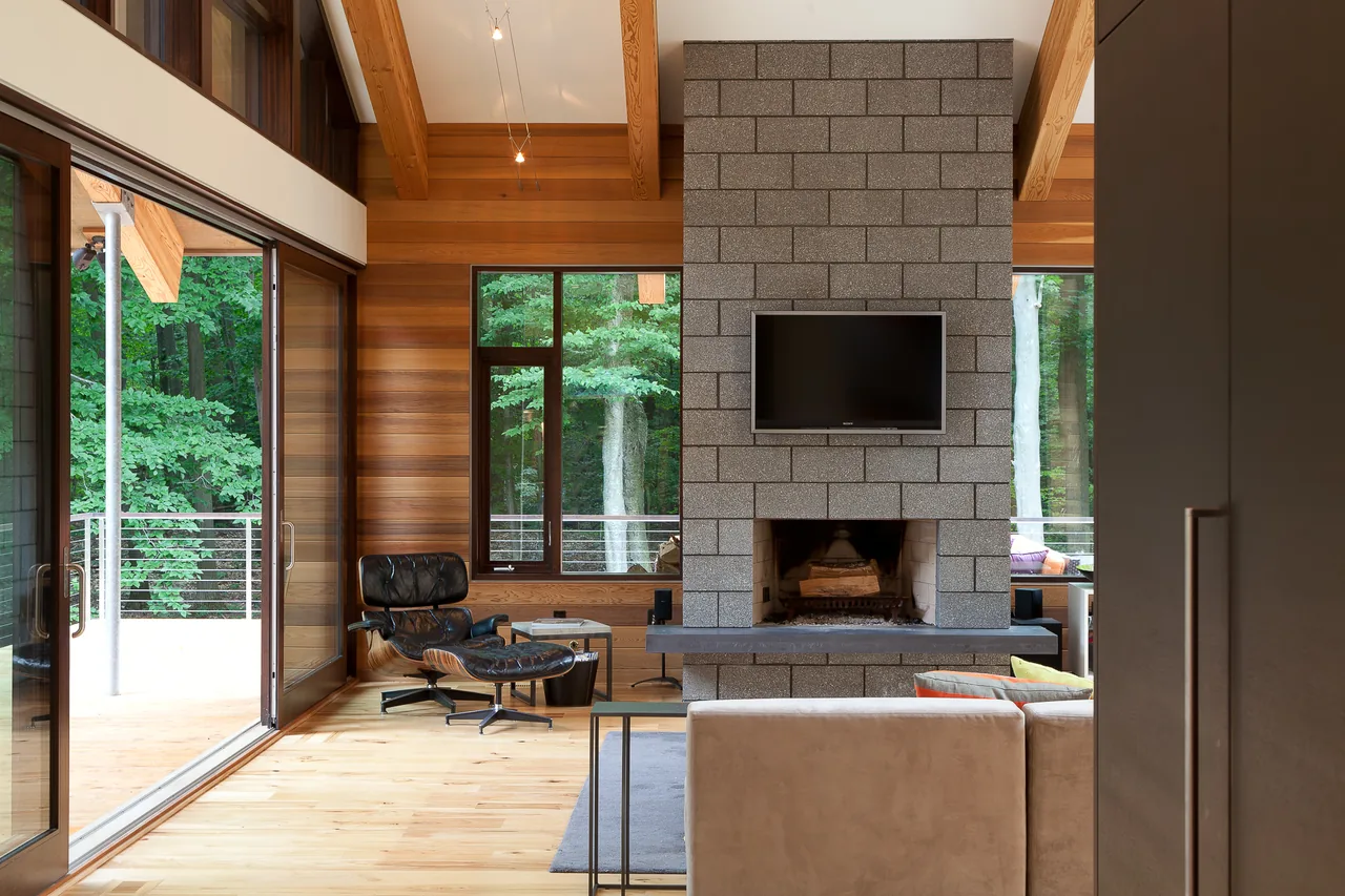 Living room of Pigeon Creek Residence features a concrete block fireplace with mounted TV, wood walls, and large sliding glass doors opening to a deck.