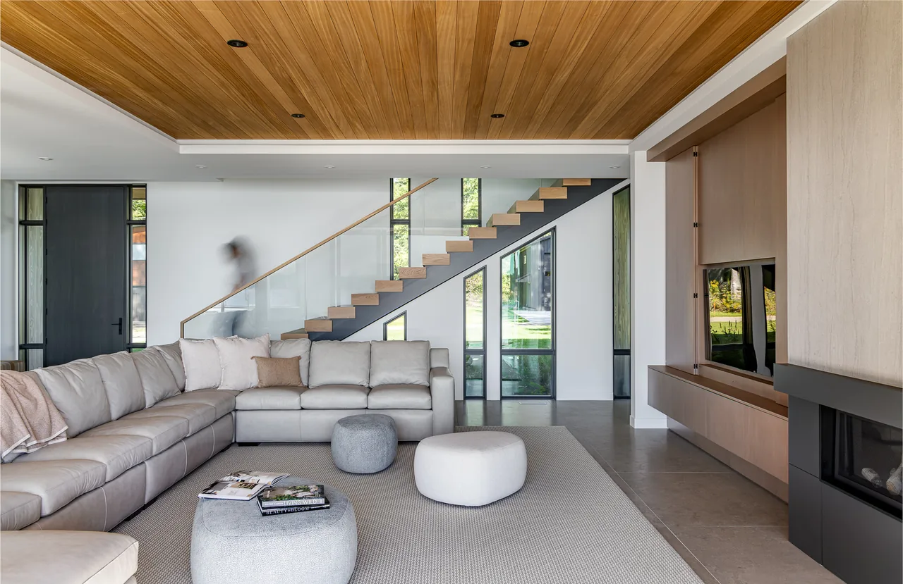 Living room of Hutchins Lakes Residence features a large sectional sofa and a staircase with glass railing.