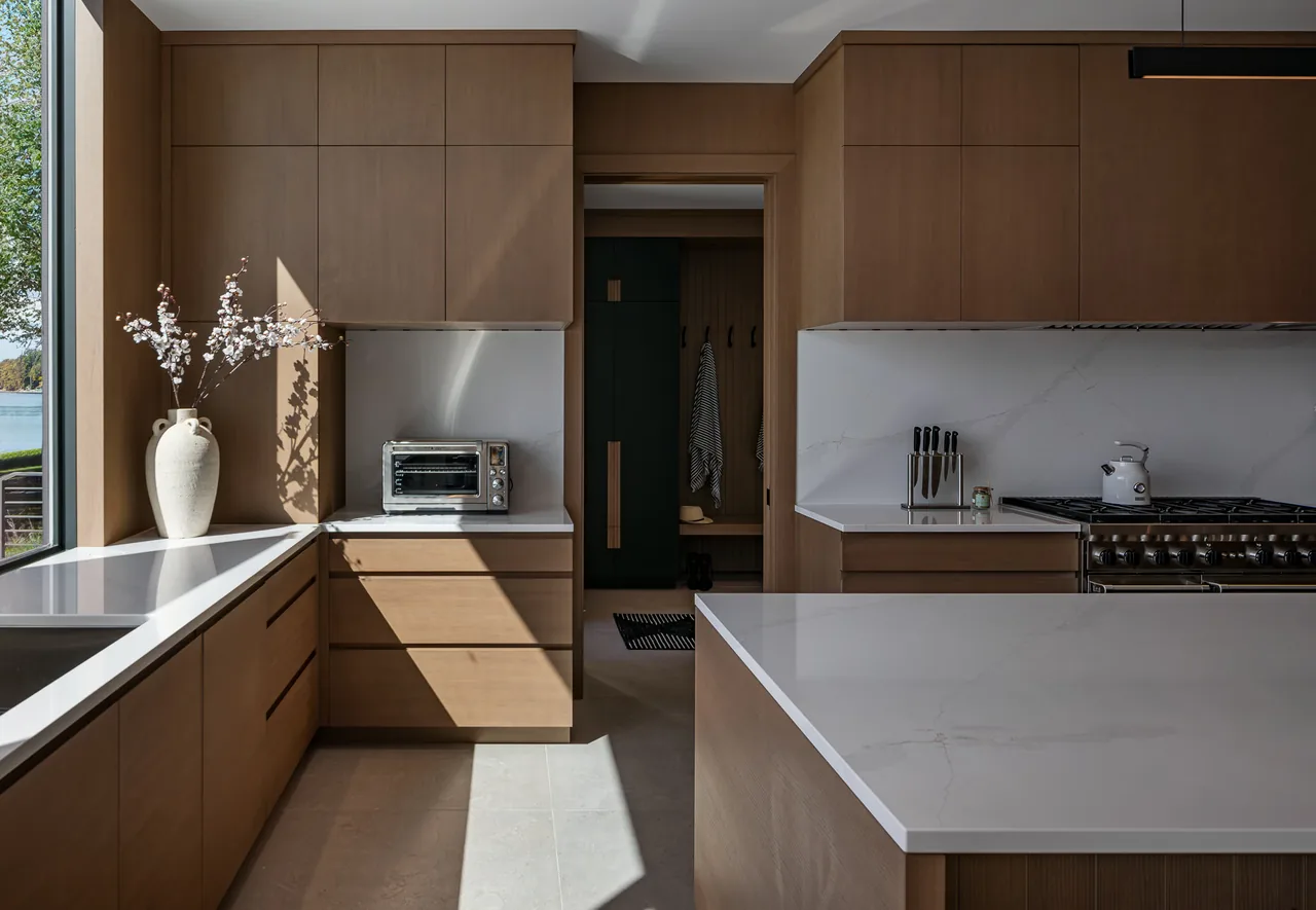 Kitchen of Hutchins Lakes Residence featuring wood cabinetry and quartz counters with lake views through a large window.
