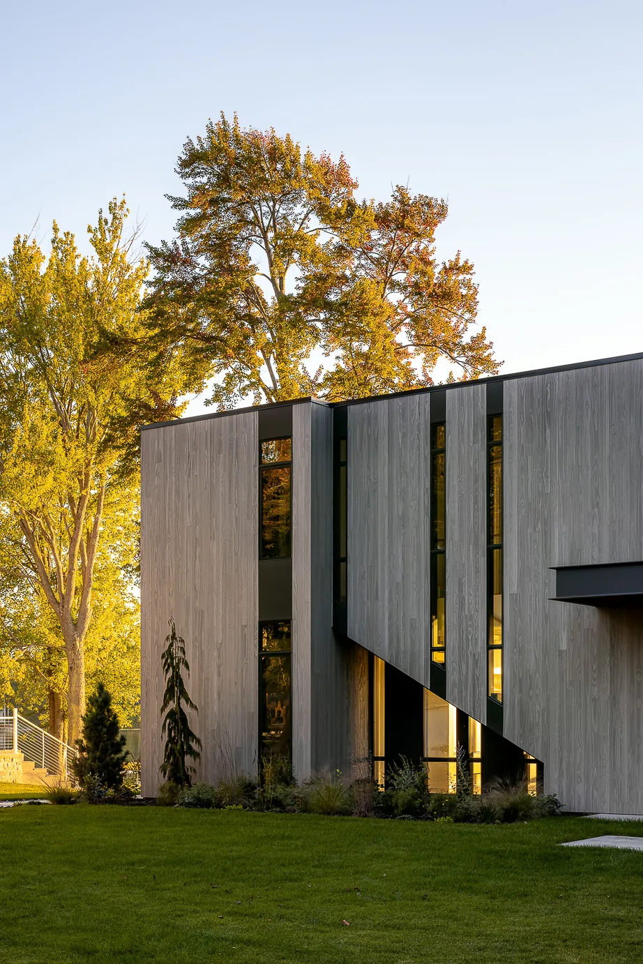 Hutchins Lakes Residence features vertical wood siding and vertical window strips with evening lighting effects.
