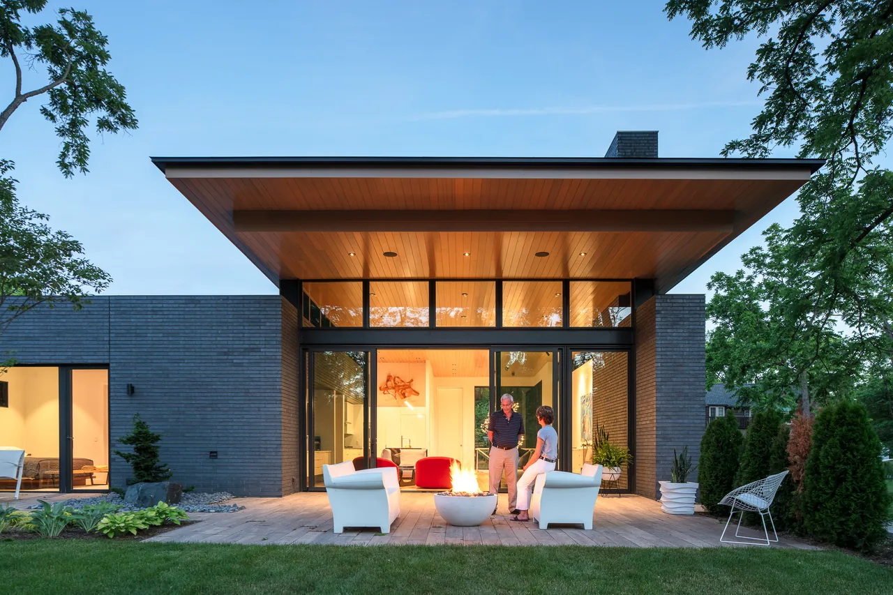 Back view of Mercer Residence showing black brick walls, wide overhang, and outdoor seating around a fire pit on the patio.