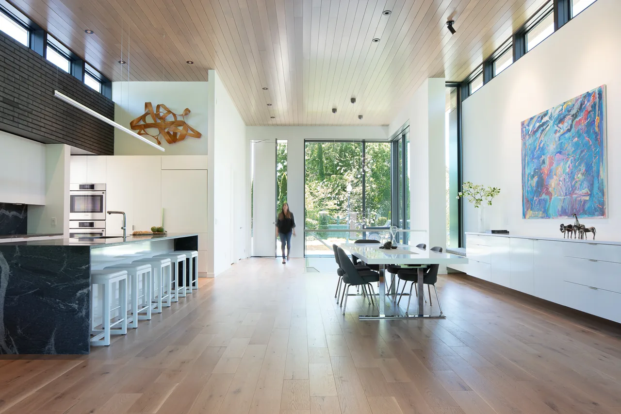 Open-plan kitchen and dining area features black marble island, white cabinetry, and expansive glazing with forest views.