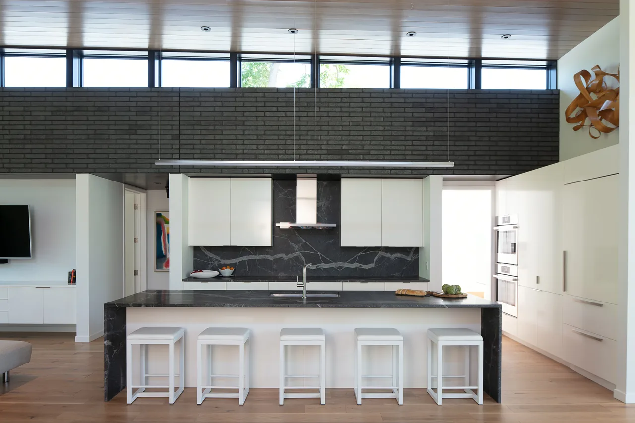 Mercer Residence kitchen features a black marble island, white cabinetry, and clerestory windows above a black brick wall.