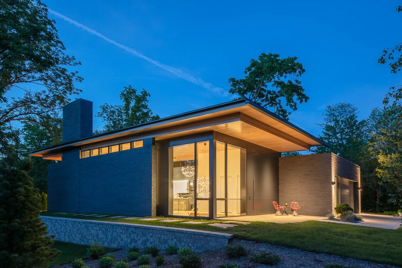 The Mercer Residence features dark brick cladding, a flat roof with wood ceiling paneling, and expansive windows under an overhang.