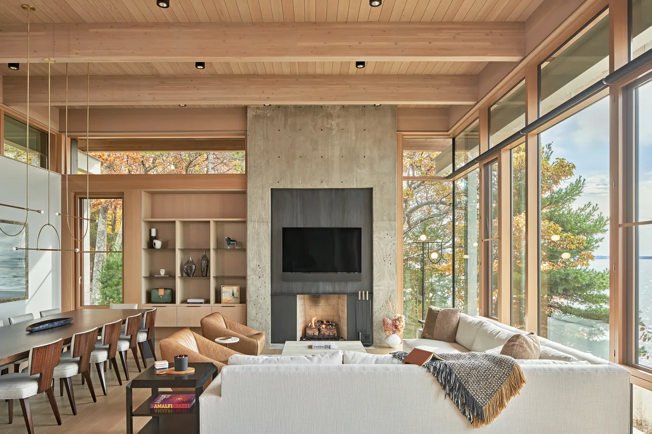 Lower Shore Residence living room shows floor-to-ceiling glazing with ocean views and a central concrete fireplace.