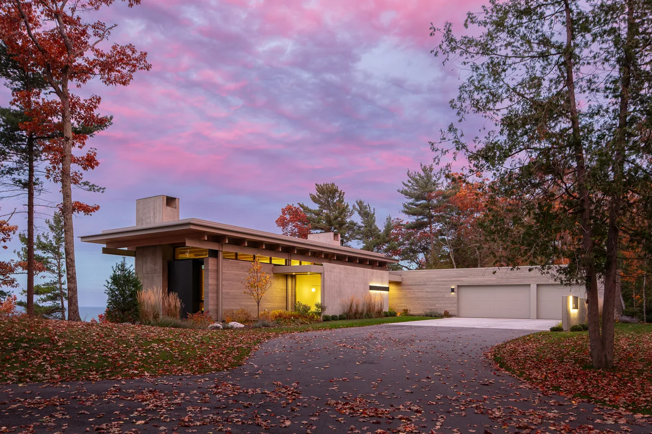 Exterior of the Lower Shore Residence by Lucid Architecture, showcasing flat roofs and concrete with wood siding, set among autumn foliage.