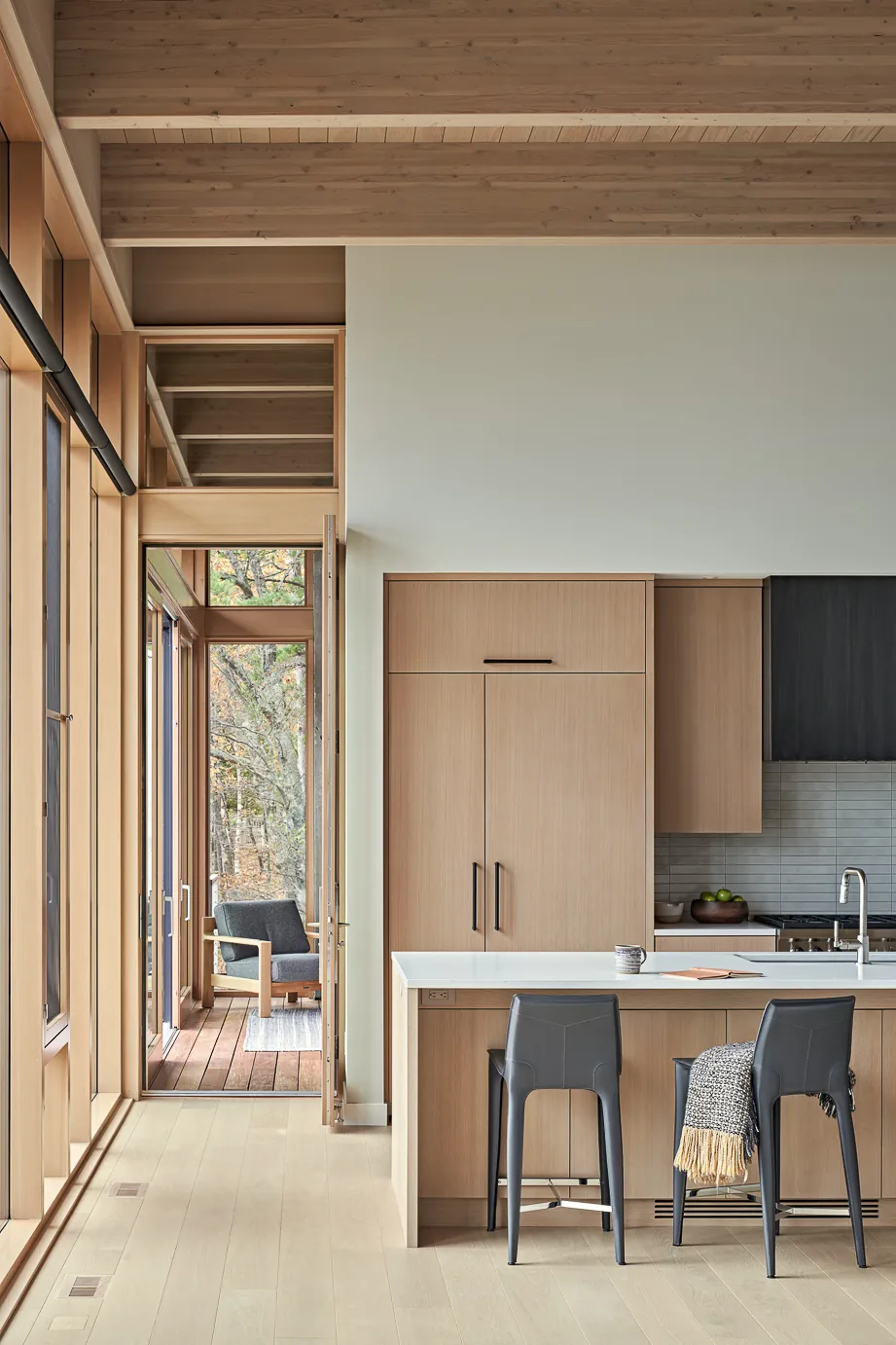 Kitchen with integrated wood cabinetry and a white island, featuring floor-to-ceiling windows opening to a covered outdoor seating area.
