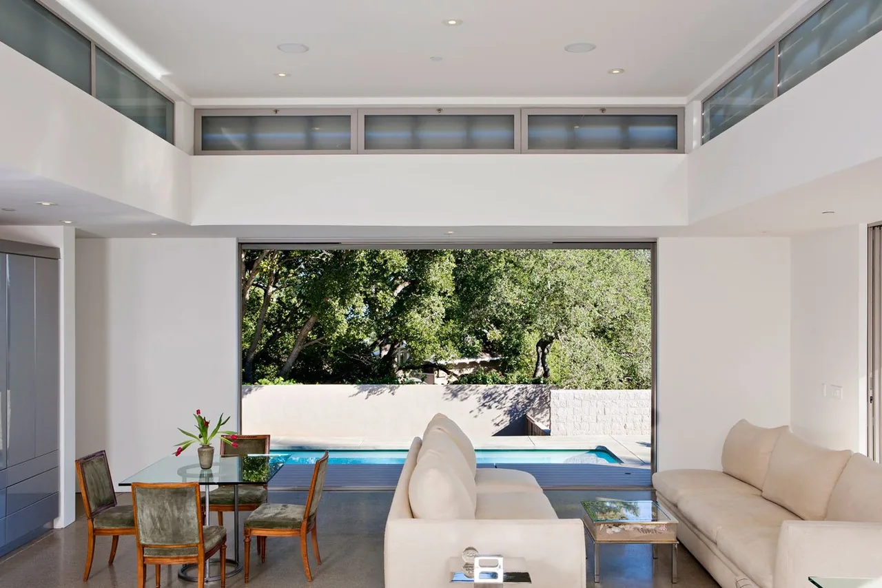 The Olson Residence living space features expansive sliding glass doors that frame a pool and outdoor greenery.