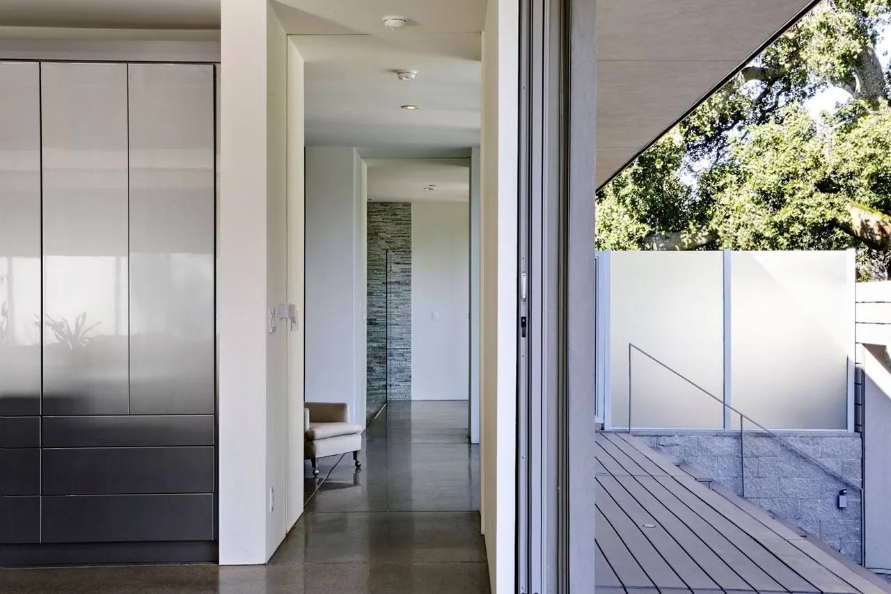 Interior hallway of Olson Residence with polished concrete flooring and built-in cabinet, leading to an outdoor deck with frosted glass panels.