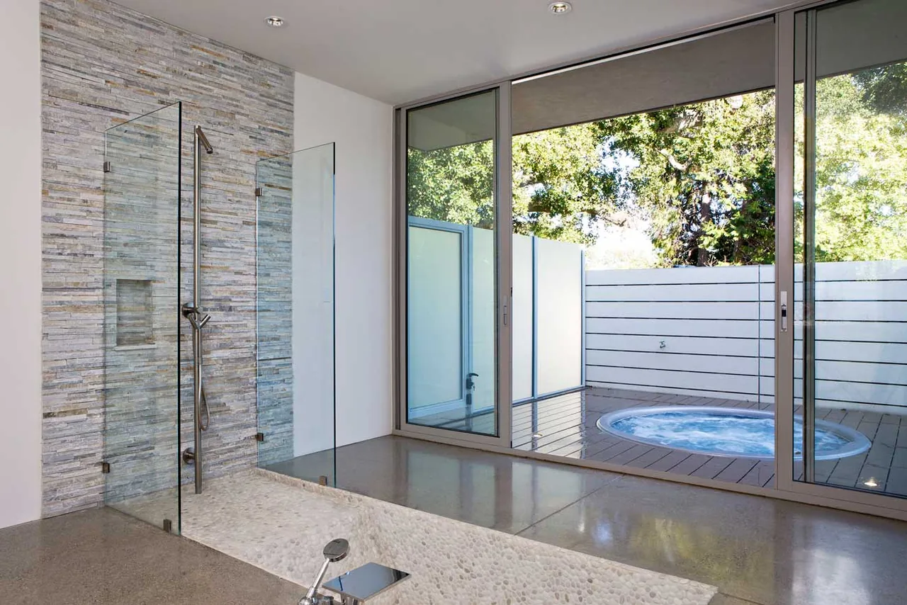 Bathroom features stone tiled shower and floor-to-ceiling sliding glass door opening to private outdoor area with hot tub.