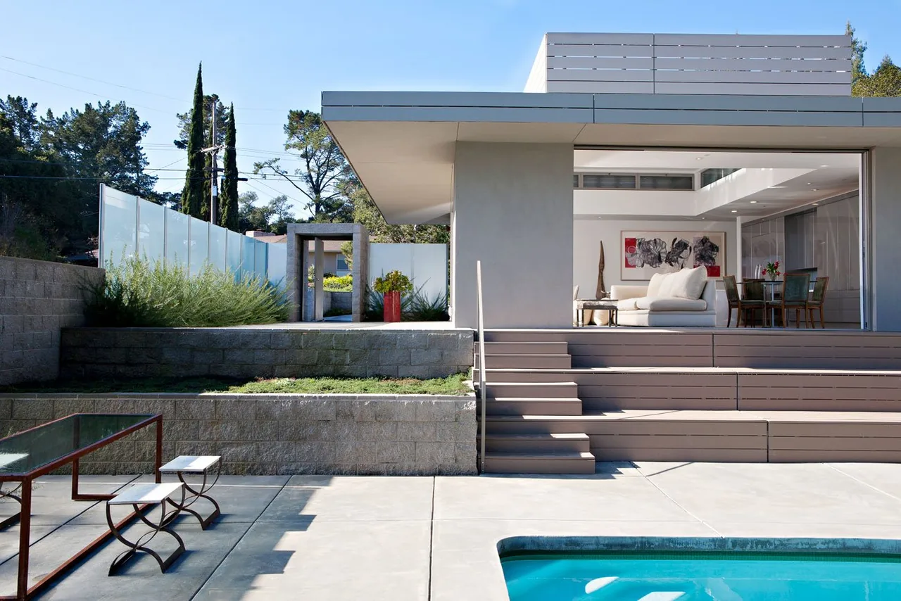 Olson Residence by Macy Architecture features a modern exterior with an open living and dining space adjacent to a pool and tiered patio.
