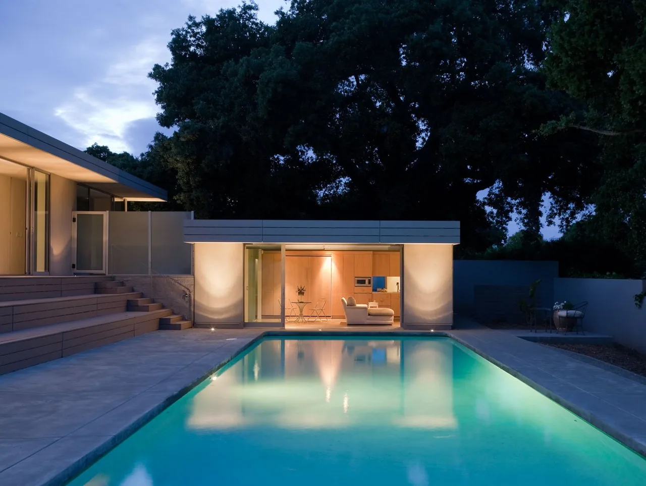 The Olson Residence by Macy Architecture features a tiered concrete patio and a pool reflecting evening lights.