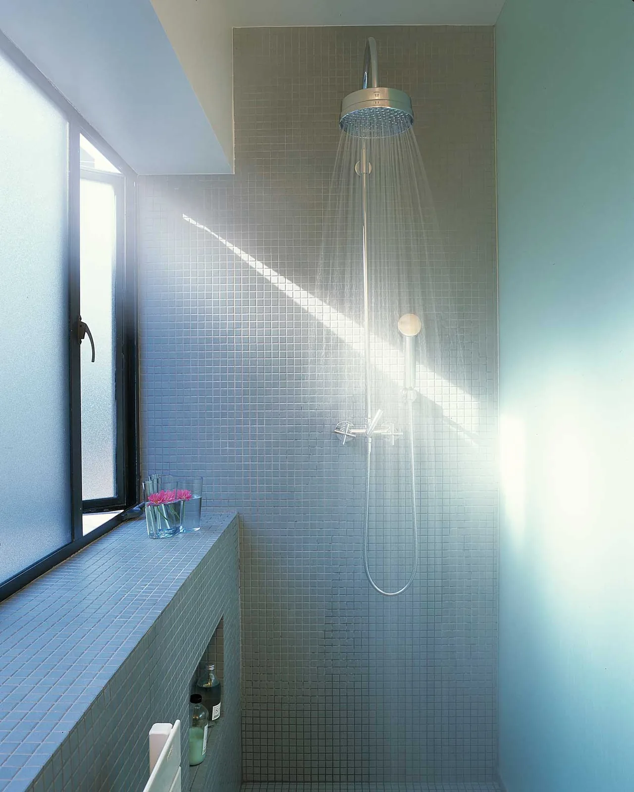 The Joss Residence shower area features small square tiles and a wall-mounted showerhead with a frosted glass window for natural light.
