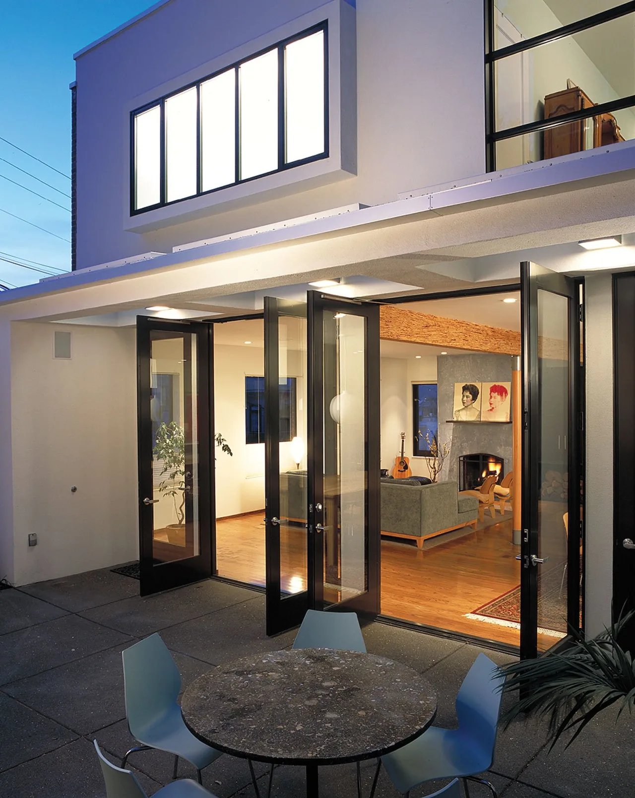 Joss Residence features folding glass doors connecting the outdoor patio to the indoor living room with a fireplace.