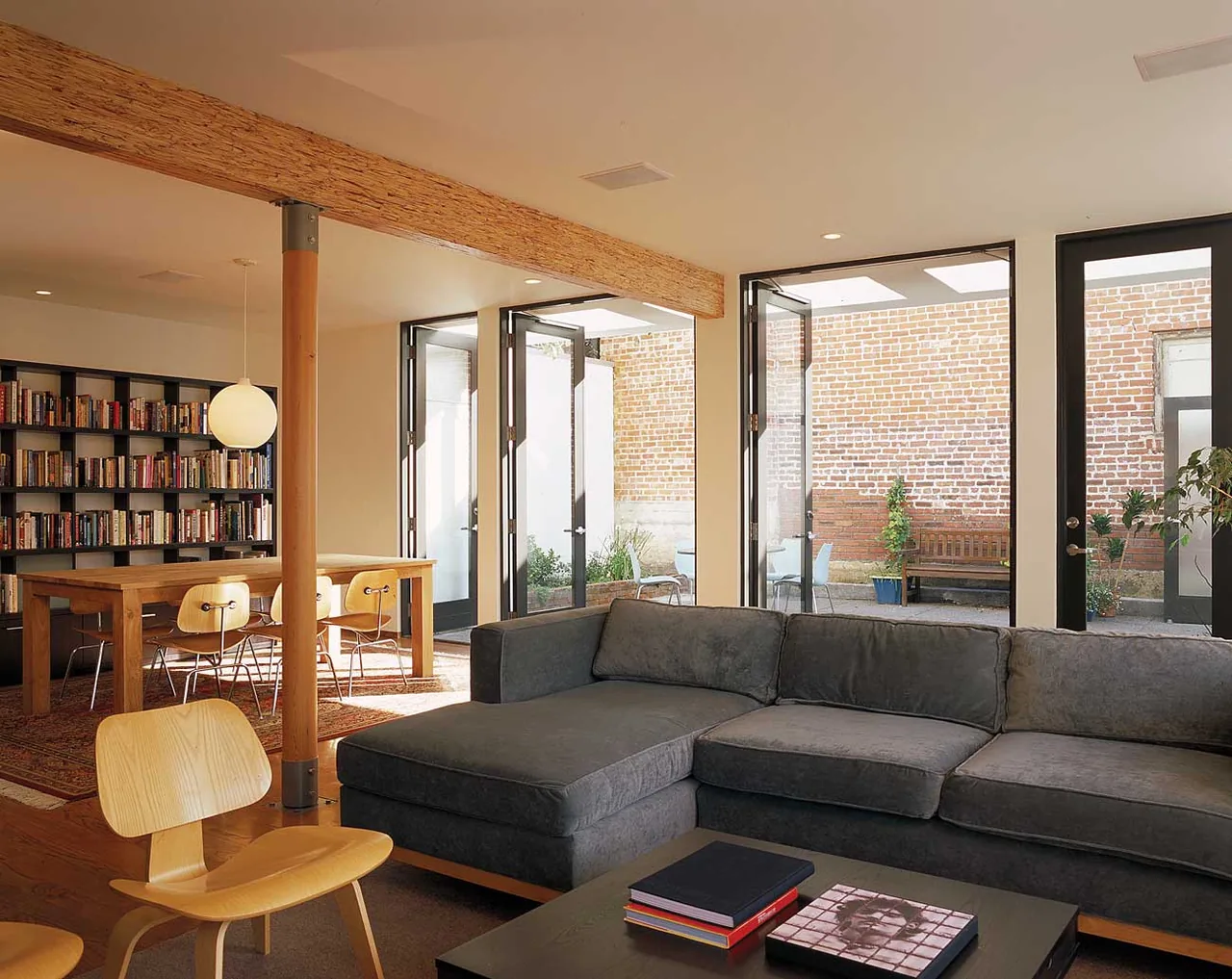Joss Residence living room features a sectional couch and opens to a brick-walled courtyard with black-framed glass doors.