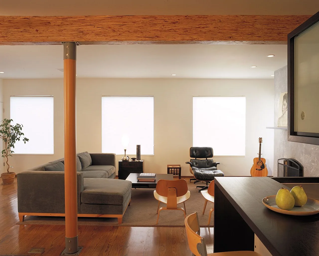 Living room with exposed wood beam, minimalist furniture, and three windows with blinds at the Joss Residence by Macy Architecture.