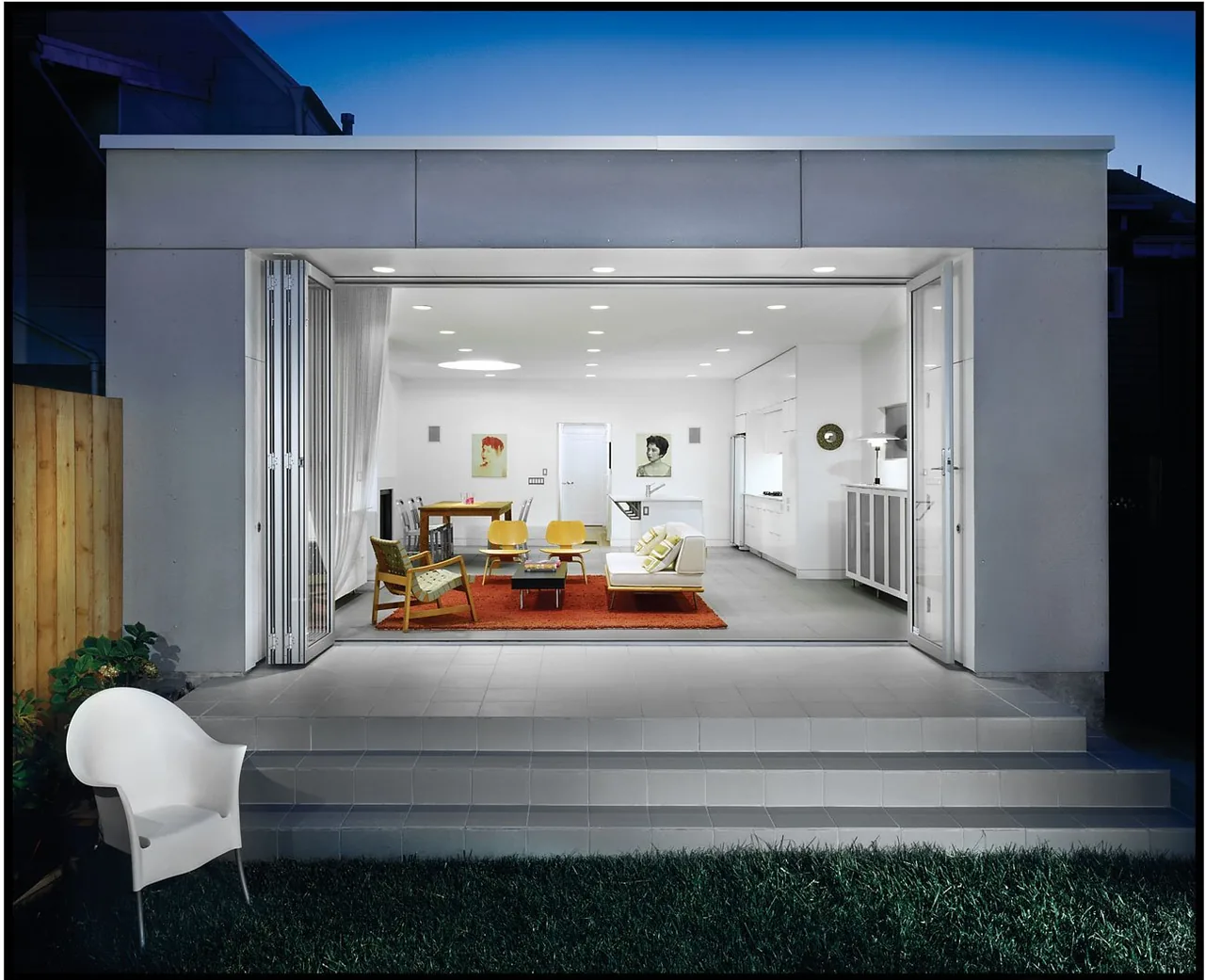 The Cabral Residence by Macy Architecture features a modern open-plan living space with folding glass doors opening to the exterior at night.
