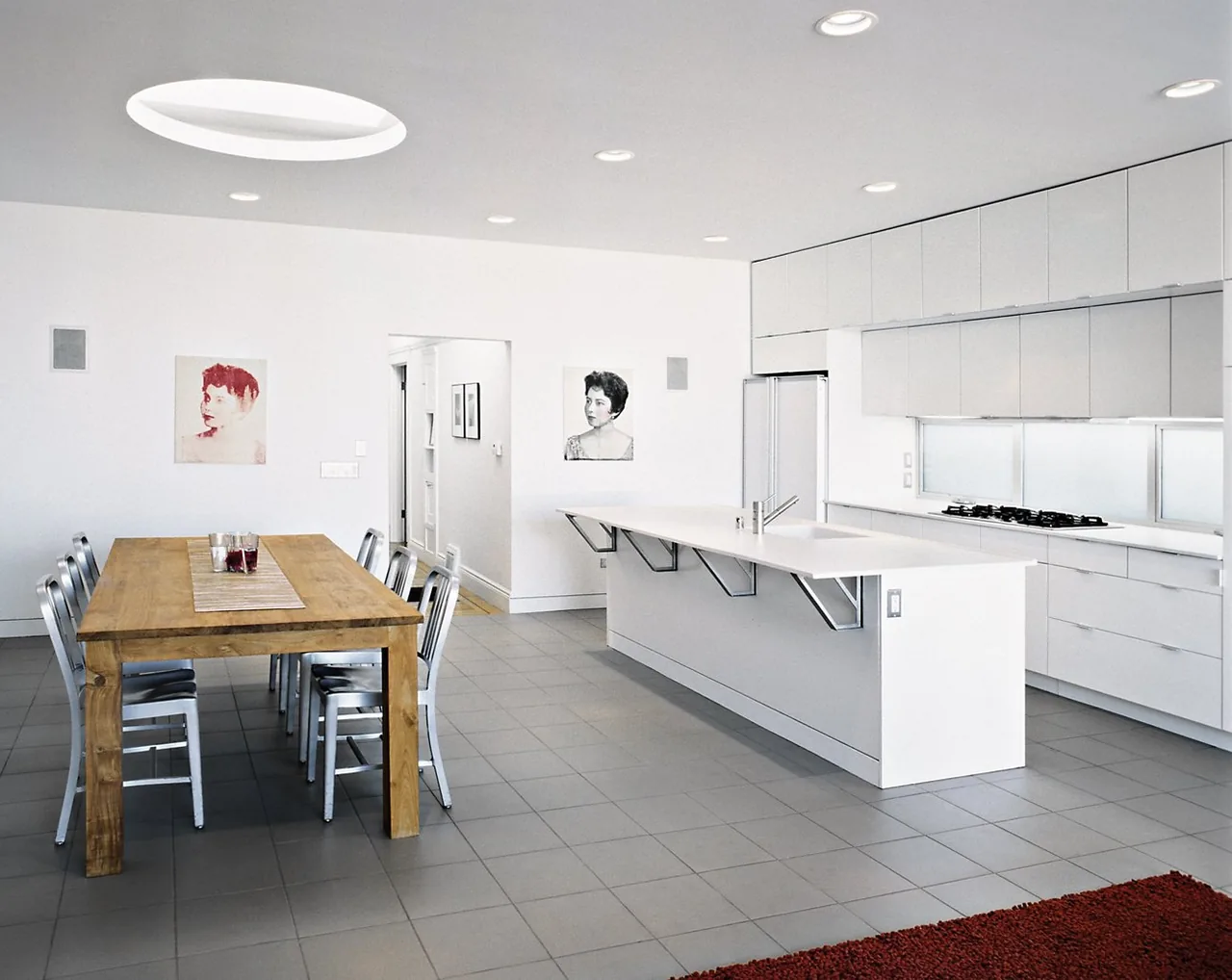 Open kitchen and dining area in the Cabral Residence features white cabinetry and a wood dining table.