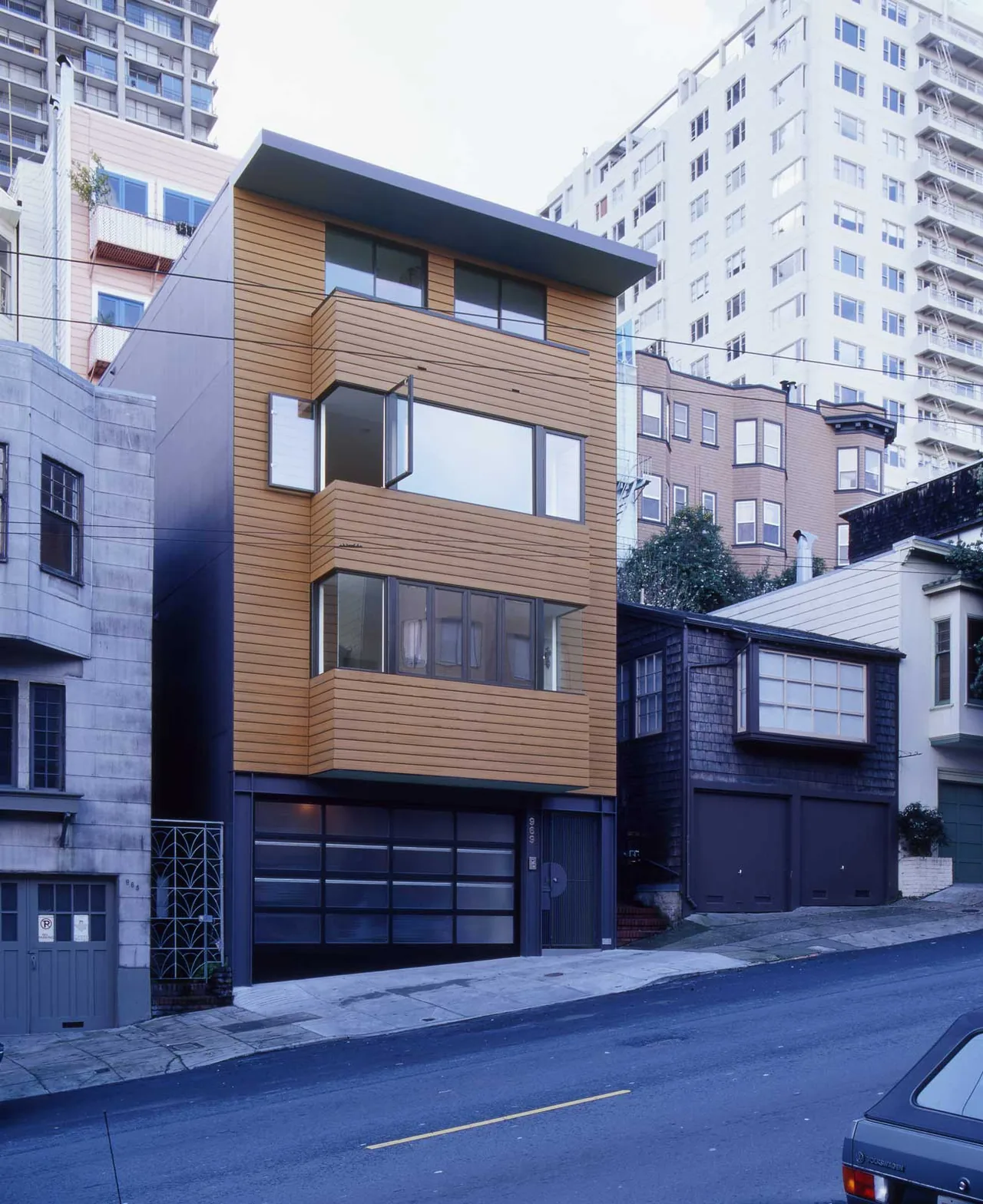 The Fisher Residence features horizontal wood siding, large black-framed windows, and a flat roof in a steep urban setting.