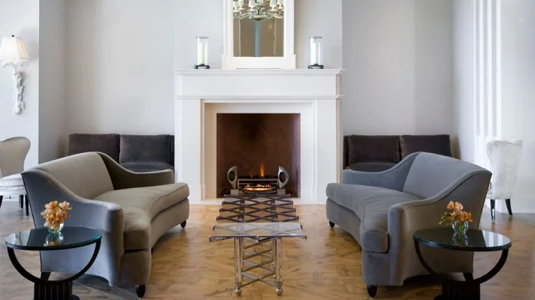 Living room featuring a white fireplace, two gray curved sofas, and a distinctive metal and glass coffee table.