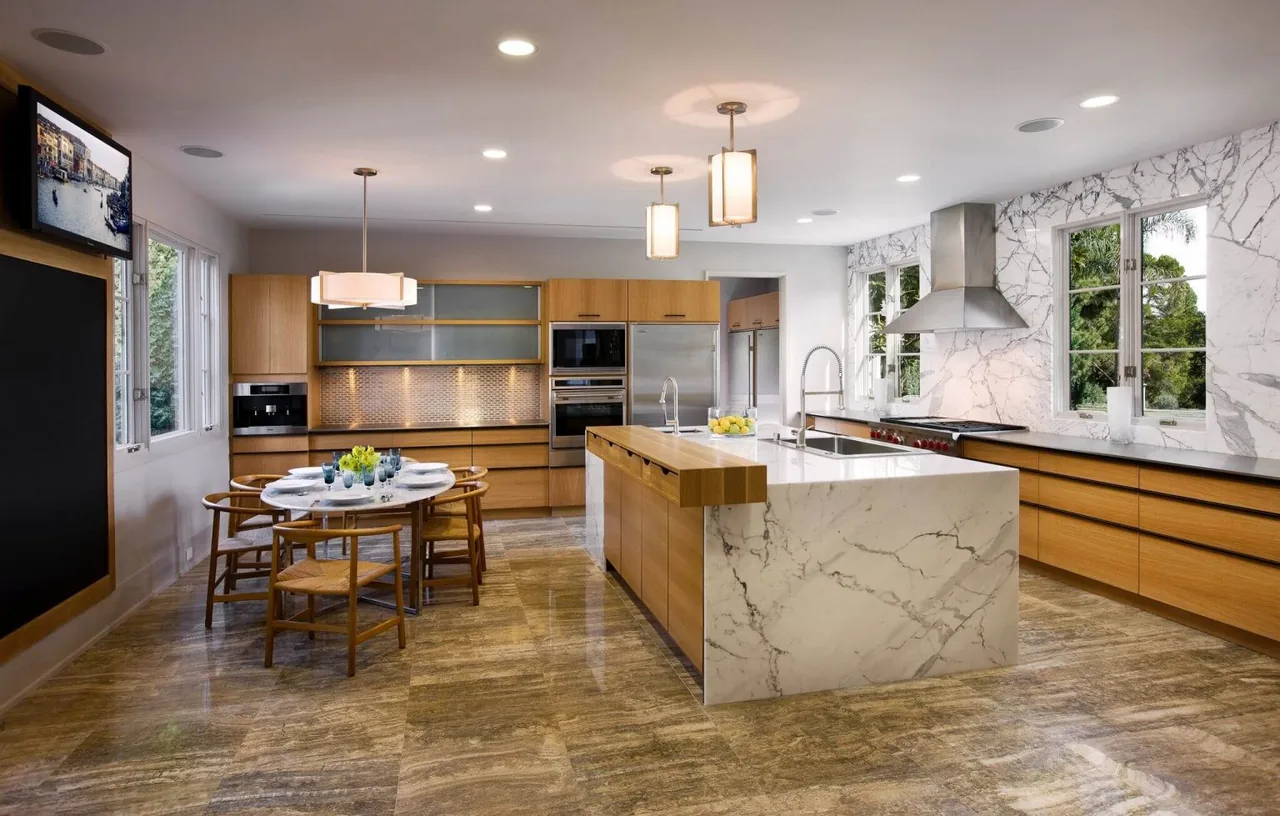 Modern kitchen features a marble island, wood cabinets, stainless steel appliances, and pendant lighting above the dining area.