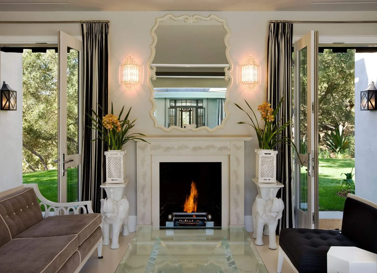Living room features a lit fireplace with decorative mantel, open glass doors to outside, and symmetrical seating arrangement.